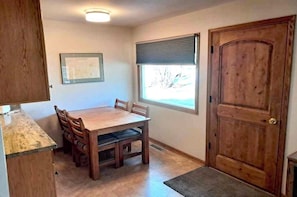 Un coin repas avec une table et des chaises en bois, une fenêtre avec des stores et une porte en bois.