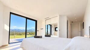 A modern bedroom with a large bed, a view of the countryside, and a sliding glass door leading to an outdoor area. - Villa Casa Di Pinarellu (Zonza)
