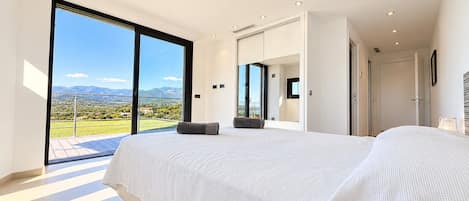 A modern bedroom with a large bed, a view of the countryside, and a sliding glass door leading to an outdoor area.