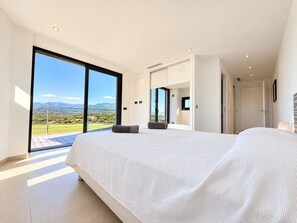 A modern bedroom with a large bed, a view of the countryside, and a sliding glass door leading to an outdoor area. - Villa Casa Di Pinarellu (Zonza)
