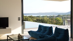 A modern living room with a glass coffee table, two blue sofas, and a flat-screen TV on a white cabinet.