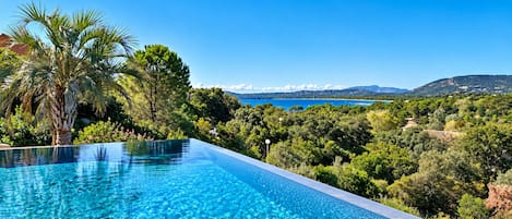 An infinity pool with a clear view of a mountainous landscape and a body of water.