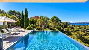 A swimming pool with lounge chairs and a wooden deck, surrounded by greenery and a view of the sea. - Villa Casa Di Pinarellu (Zonza)