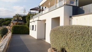 A modern building with a balcony, a wooden deck, and well-maintained hedges.