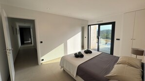 A bedroom with a bed, a view through a sliding glass door, and a hallway leading to another room.