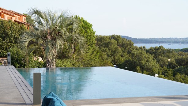 A pool with a wooden deck and a view of a forest and water.
