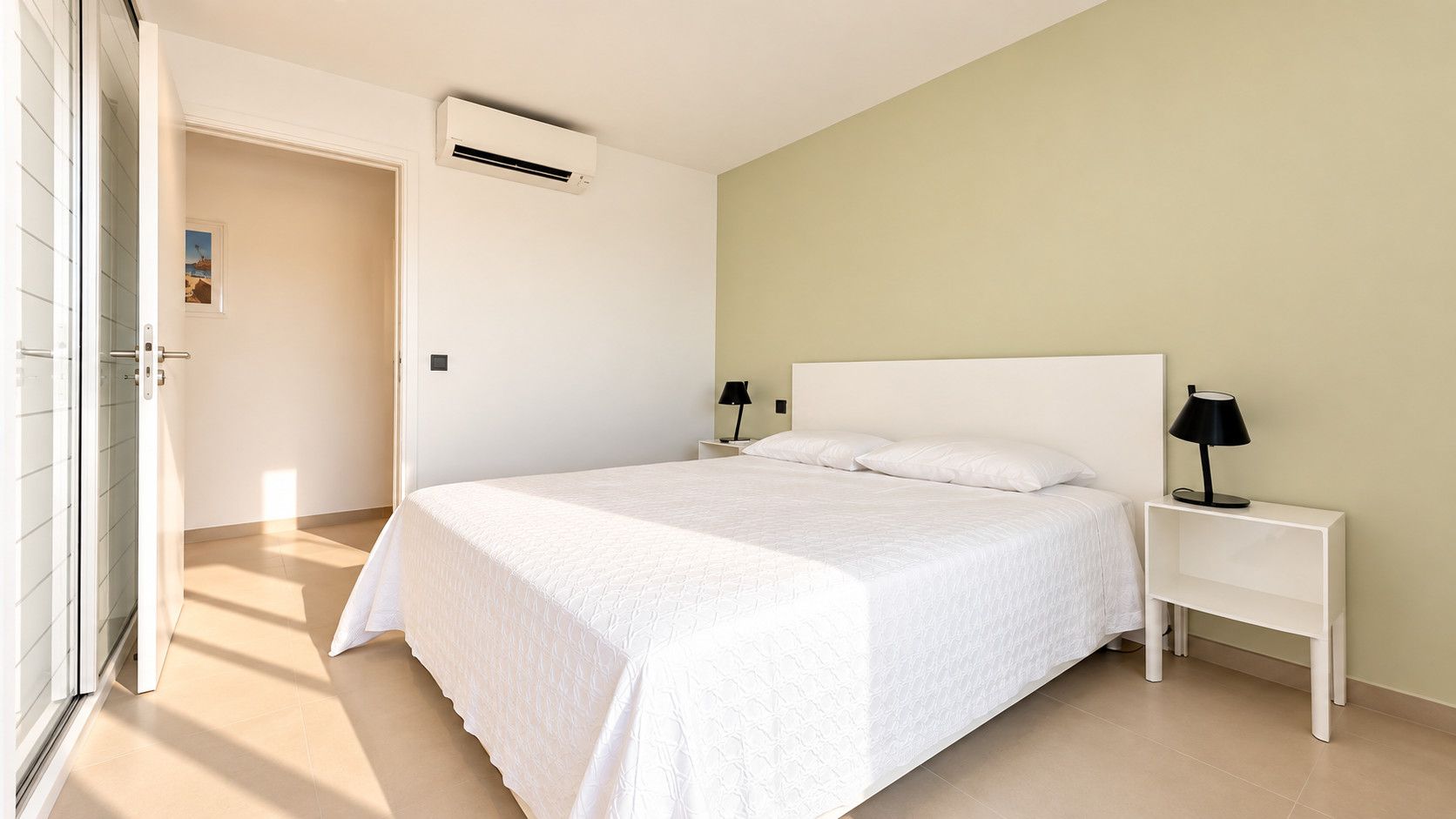 Une chambre à coucher comprenant un lit, des tables de chevet, un appareil de climatisation et une porte donnant sur une autre pièce.