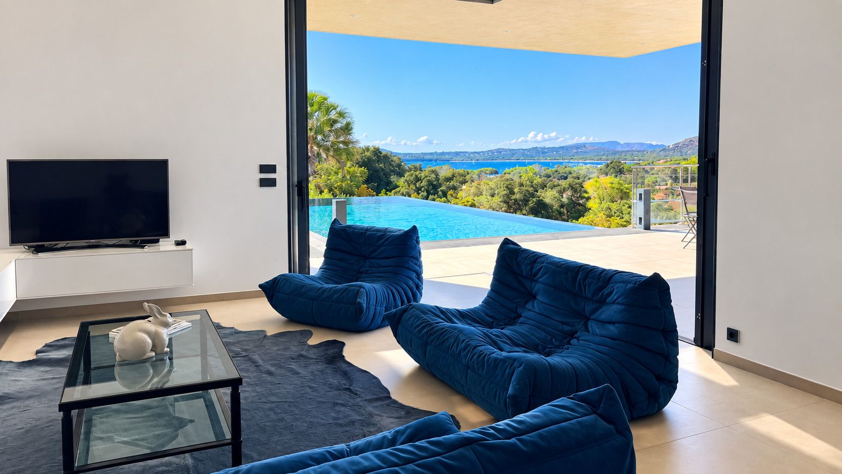 A modern living room with a large window, a flat-screen TV, and a pool view.