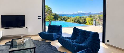 A modern living room with a large window, a flat-screen TV, and a pool view.