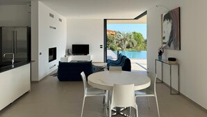 A modern kitchen with a built-in refrigerator, a flat-screen TV, and a dining area with a round table and white chairs.