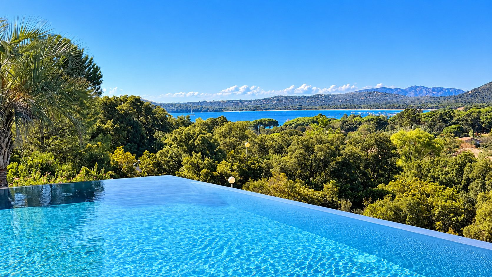 An infinity pool with a clear view of a lake and mountains in the background.
