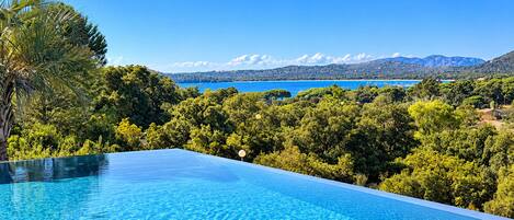 An infinity pool with a clear view of a lake and mountains in the background.