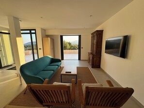 A modern living room with a teal sofa, wooden chairs, a small table, and a TV mounted on the wall. - Villa Roma Di Pinarellu (Zonza)