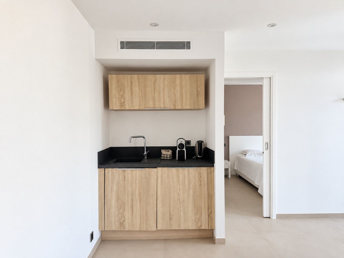 A compact kitchen with a black countertop, wooden cabinets, and a built-in vent.