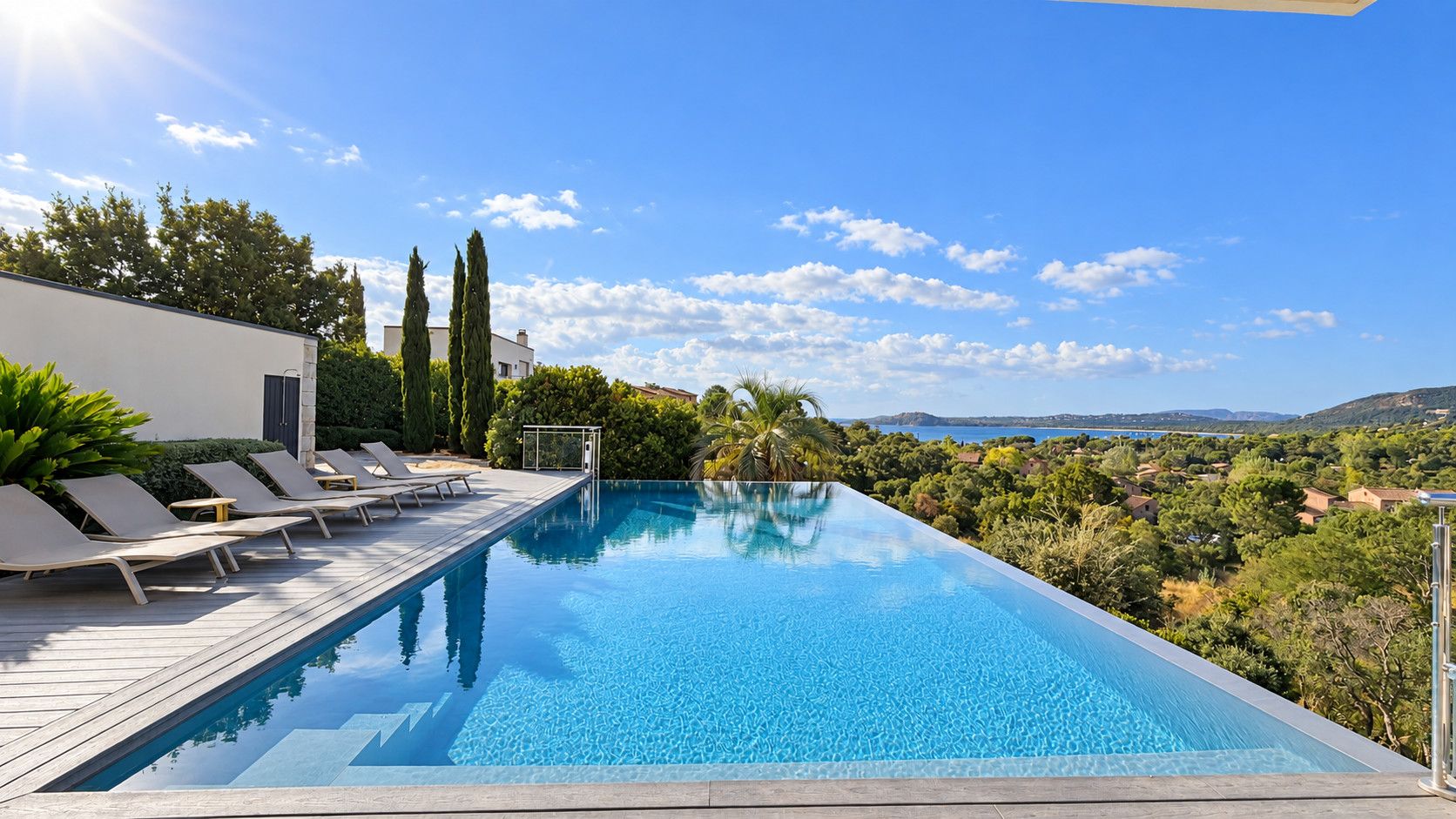 Ein rechteckiger Infinity-Pool mit einer Holzterrasse und Liegestühlen, umgeben von viel Grün und mit Blick auf eine schöne Landschaft.