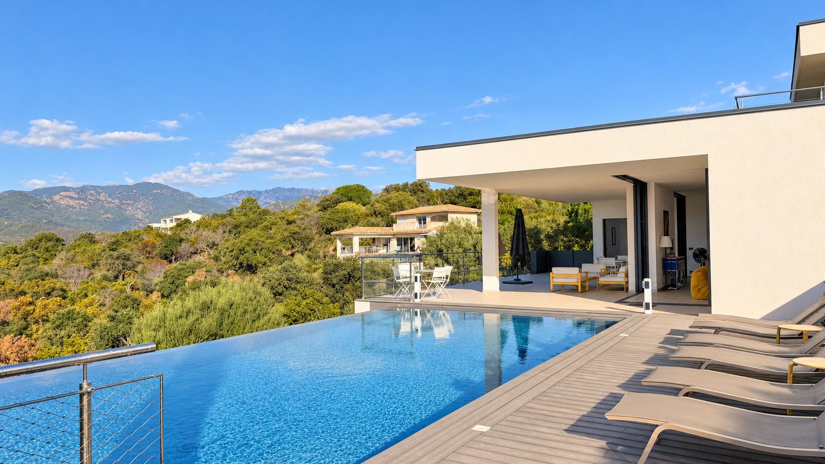 A modern pool area with a clear view of the surrounding landscape, including distant mountains and a villa.