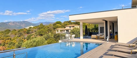 A modern pool area with a clear view of the surrounding landscape, including distant mountains and a villa.