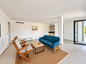 A modern living room with a sofa, a wooden chair, a small table, and a kitchen in the background. - Villa Roma Di Pinarellu (Zonza)