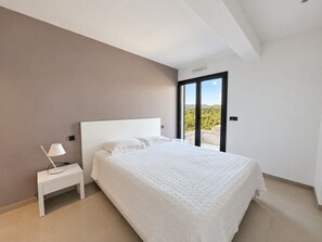 A bedroom with a bed, a nightstand, a lamp, and a sliding glass door leading to a balcony. - Villa Roma Di Pinarellu (Zonza)