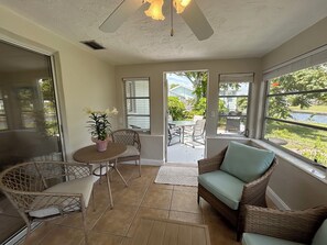 A sunroom with wicker furniture, a potted plant, and large windows offering a view of the outdoors. - Canal Front Home in Englewood (Englewood)