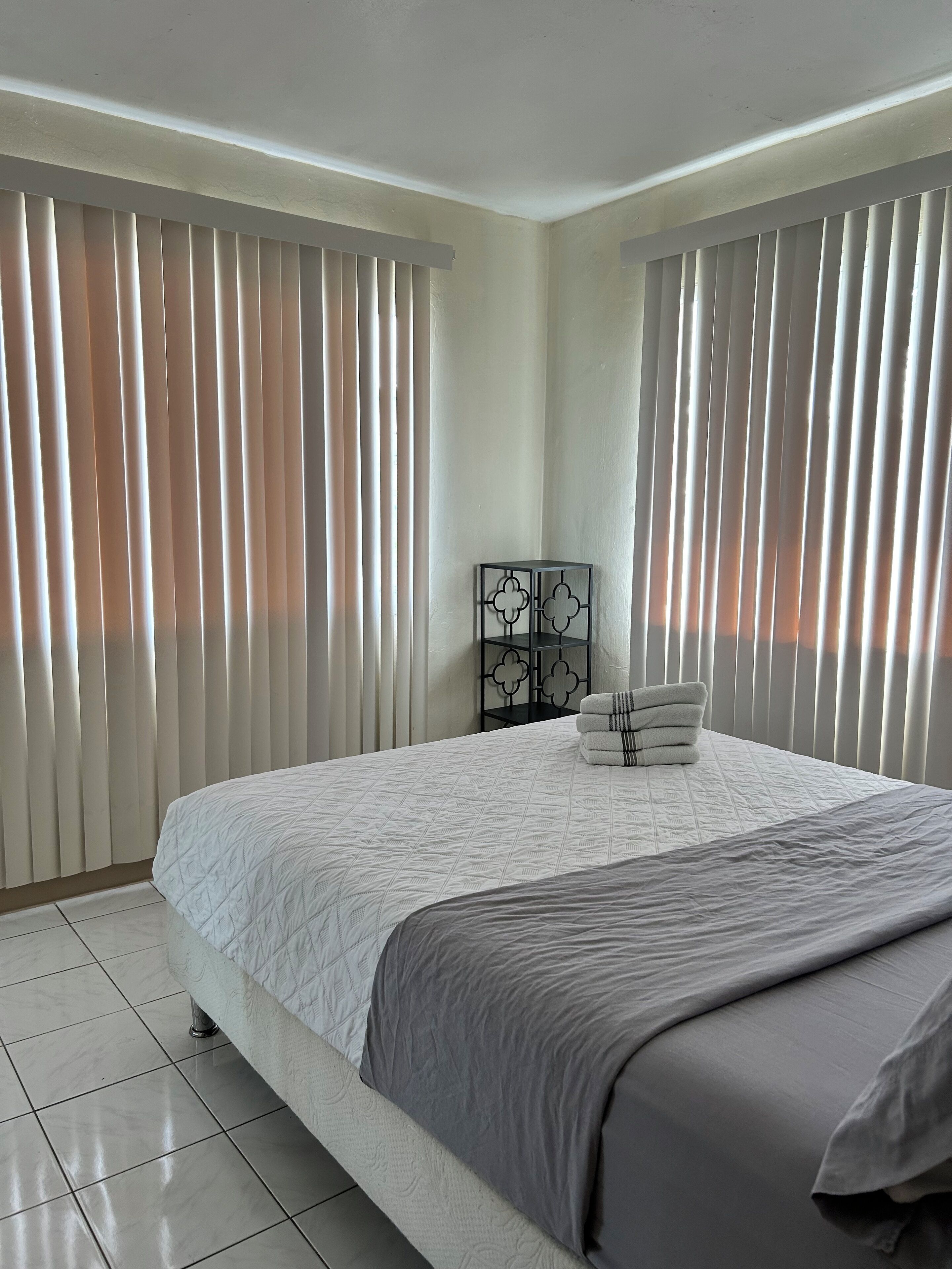 Un dormitorio moderno con una cama grande, paredes blancas y persianas verticales.
