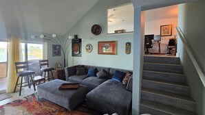 Een woonkamer met een modulaire bank, een dartbord en een televisie. Er is een trap die naar een ander niveau leidt.