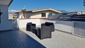 A rooftop terrace with outdoor furniture, a white wall, and a view of buildings and mountains. - Vertigo Casoria (Casoria)