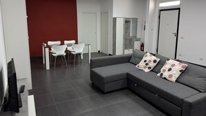 A modern living room with a grey sectional sofa, white chairs, and a red accent wall. - Vertigo Casoria (Casoria)