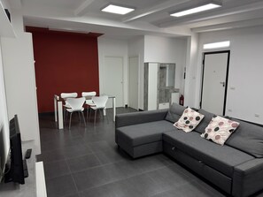 A modern living room with a grey sectional sofa, white chairs, and a red accent wall. - Vertigo Casoria (Casoria)