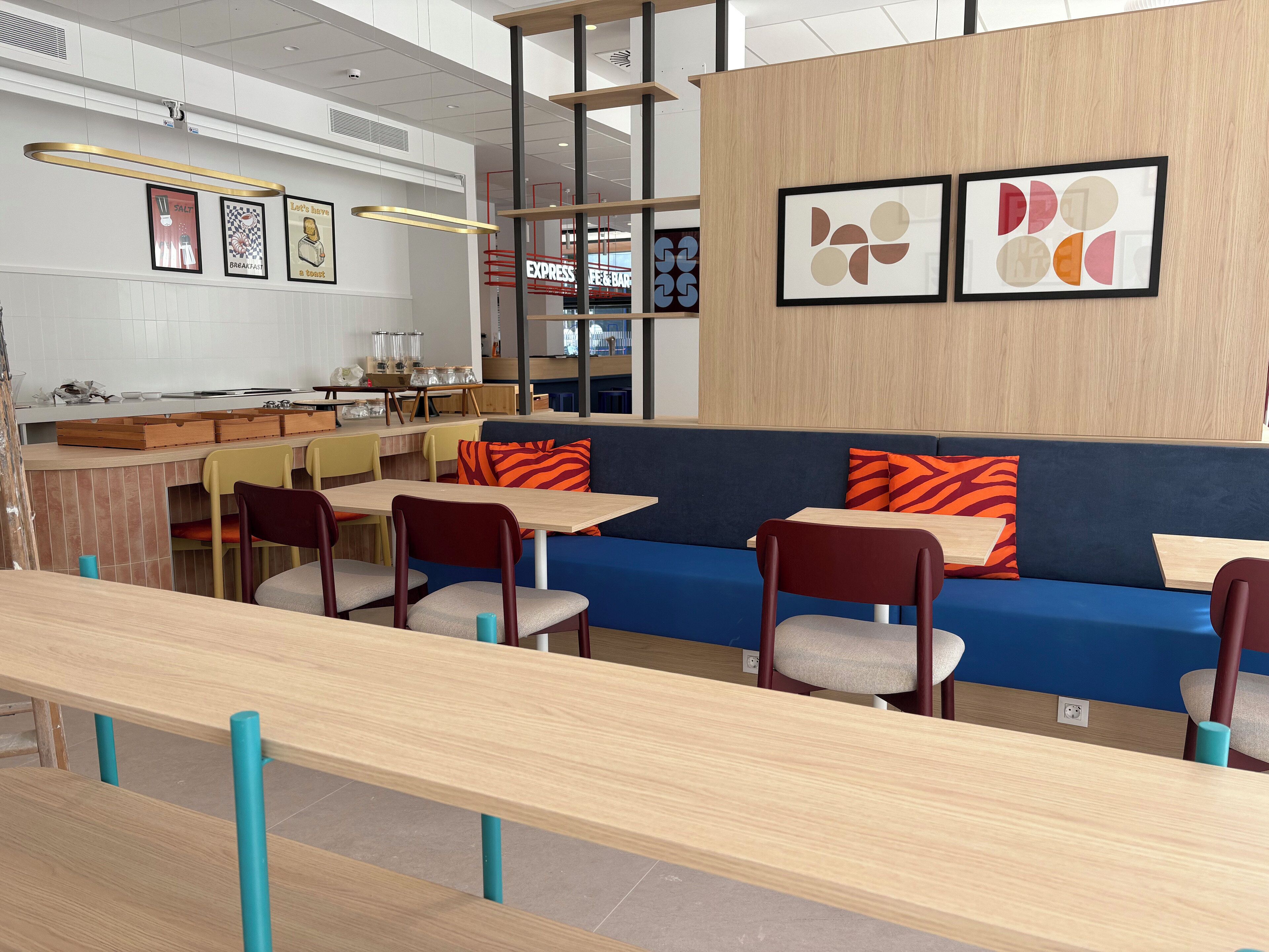 Una cafetería moderna con mesas de madera, asientos azules y obras de arte en las paredes.