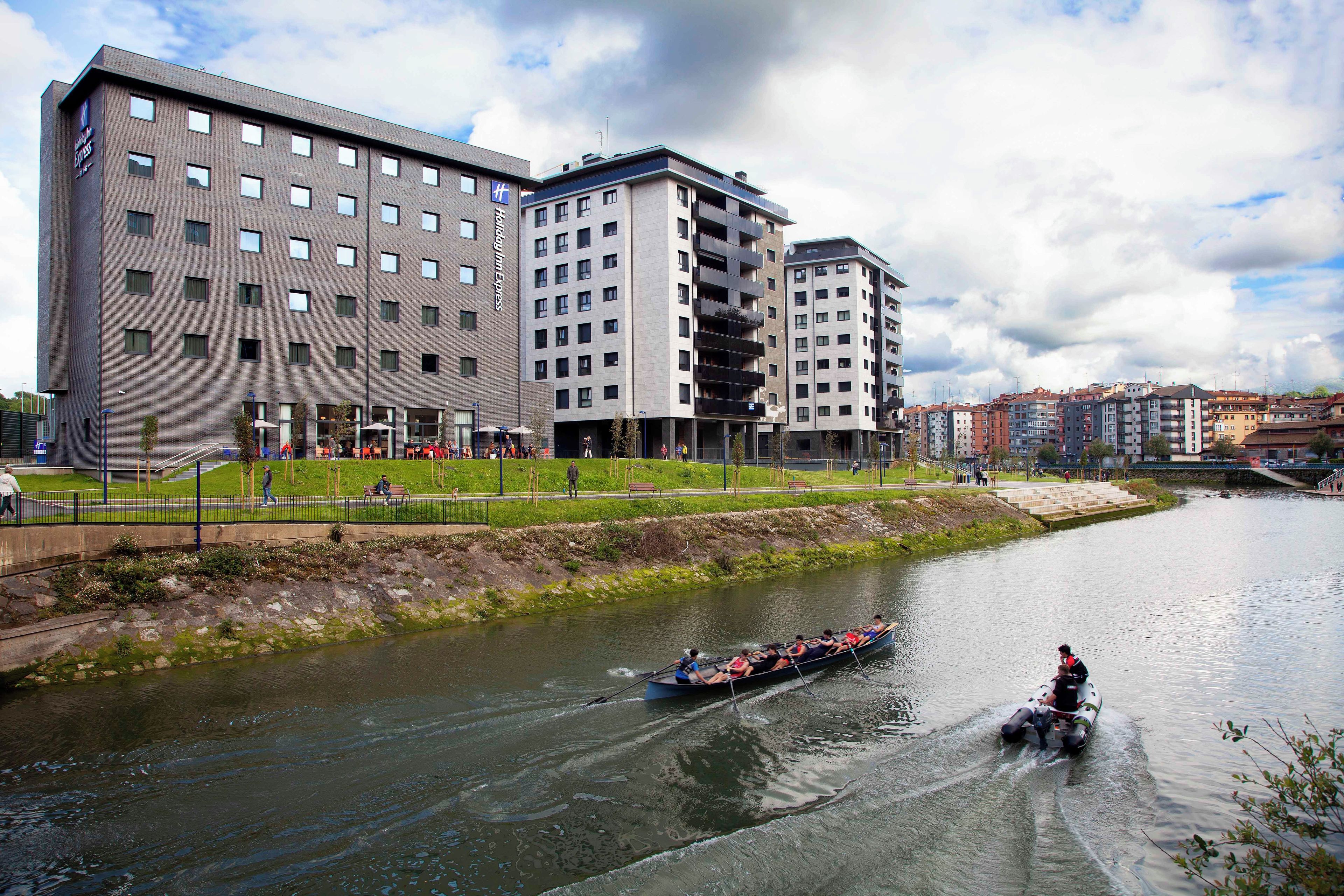 A riverside view with modern buildings and a boat with passengers.