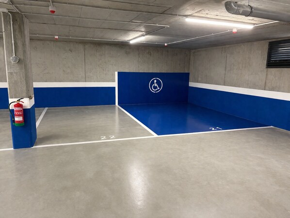Un estacionamiento con paredes pintadas de azul y blanco, un extintor montado en un pilar y un símbolo de accesibilidad para sillas de ruedas en la pared.