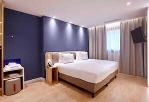A hotel room with a large bed, bedside tables, a flat-screen TV, and a window with curtains.