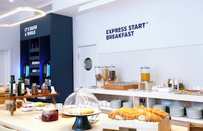 Un espace buffet pour le petit-déjeuner proposant une variété d’aliments, notamment des viennoiseries et des boissons, ainsi qu’un panneau indiquant « PETIT-DÉJEUNER EXPRESS ».