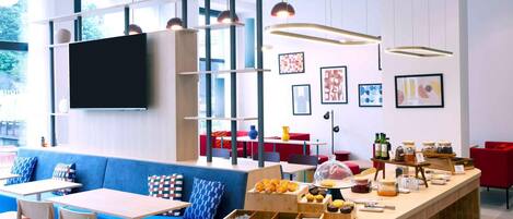 Un café moderno con un sofá azul, mesas de madera y un mostrador de buffet con pasteles.
