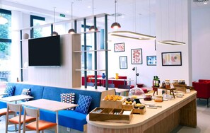 A modern cafe with a blue sofa, wooden tables, and a buffet counter with pastries.