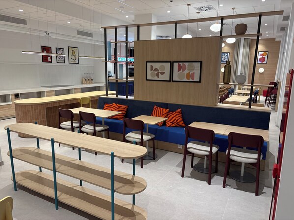A modern cafe with wooden furniture, a blue sofa with orange cushions, and a counter area.