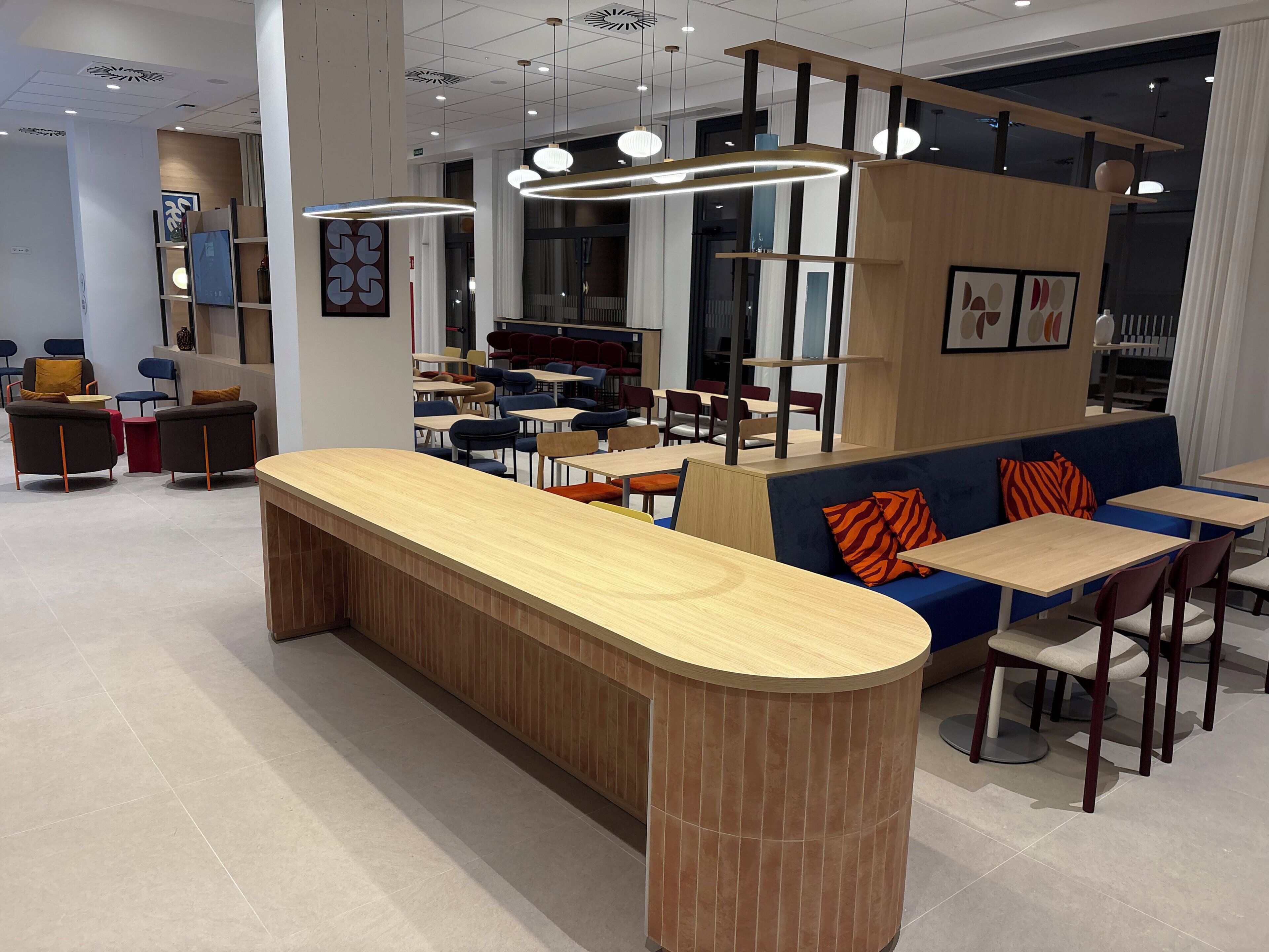 Un interior moderno con un mostrador central de madera, zonas de estar e iluminación colgante.
