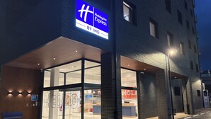 Der Eingang eines Holiday Inn Express Hotels mit Glasfassade, einem blauen Schild und einem Parkplatz.