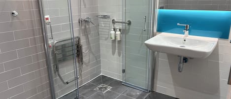 Un baño moderno con cabina de ducha de vidrio, un lavabo blanco y una pared azul decorativa.