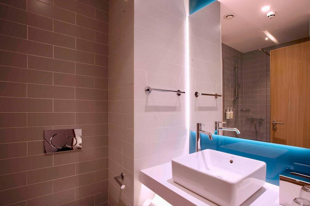 Un baño moderno con un lavabo blanco, una pared de acento azul y una cabina de ducha con mampara de vidrio.