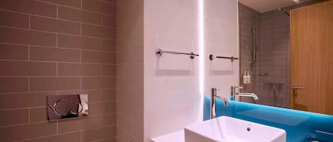 A modern bathroom with a white sink, a blue accent wall, and a glass shower enclosure.