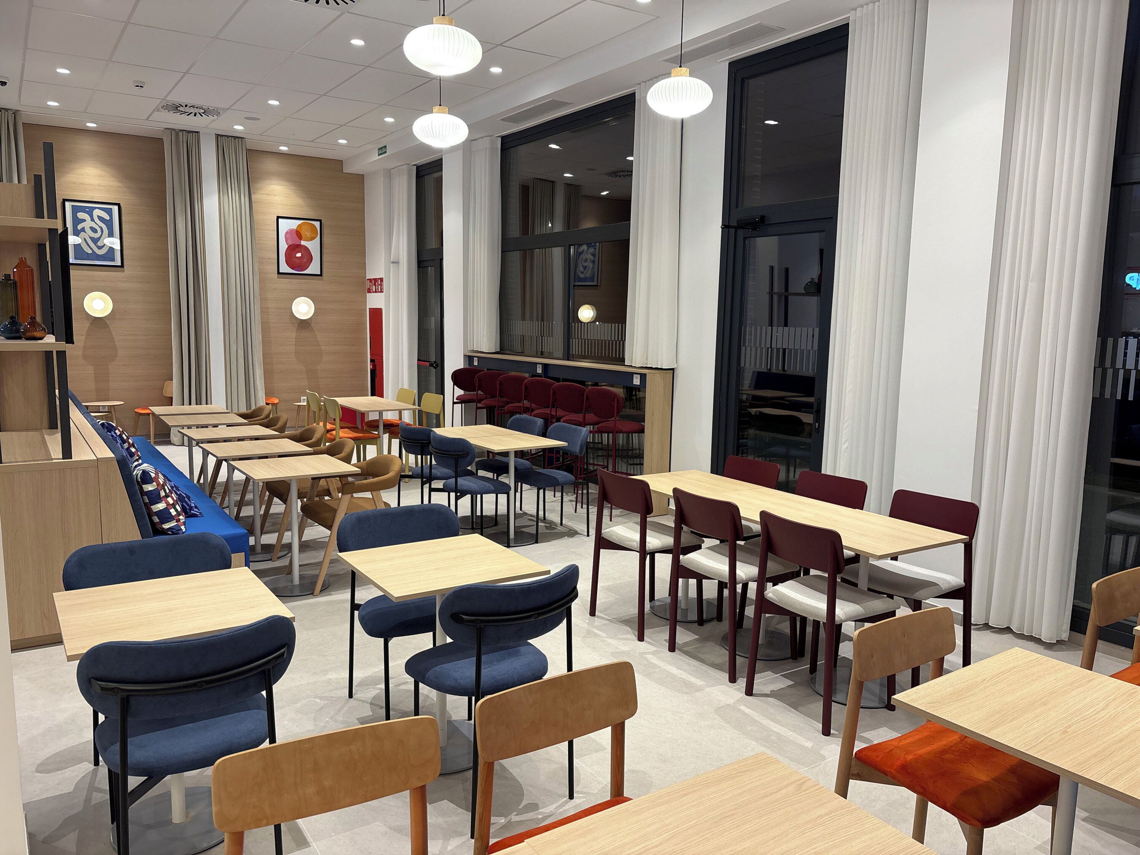 Een moderne eetruimte met tafels, stoelen, een counter en grote ramen.