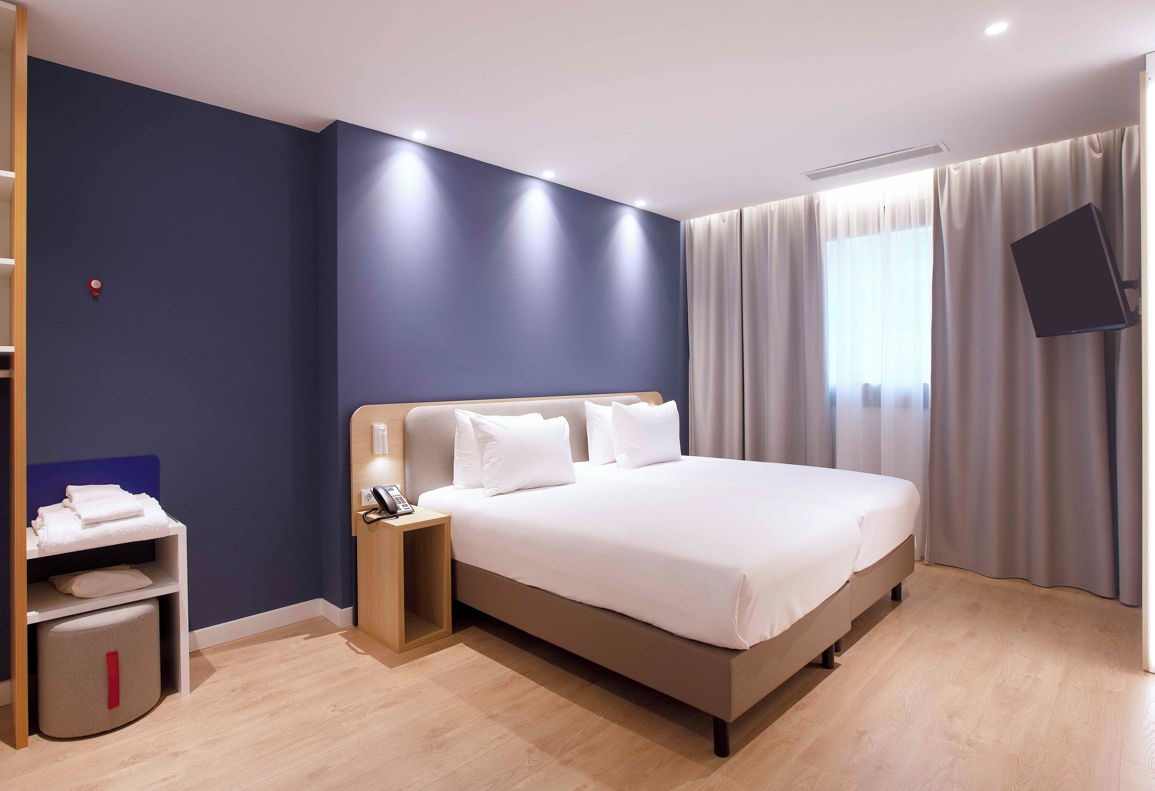 Una habitación de hotel con una cama, una mesita de noche y un televisor montado en la pared.