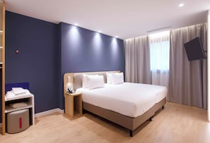 Une chambre d’hôtel avec un lit, une table de chevet et un téléviseur fixé au mur.