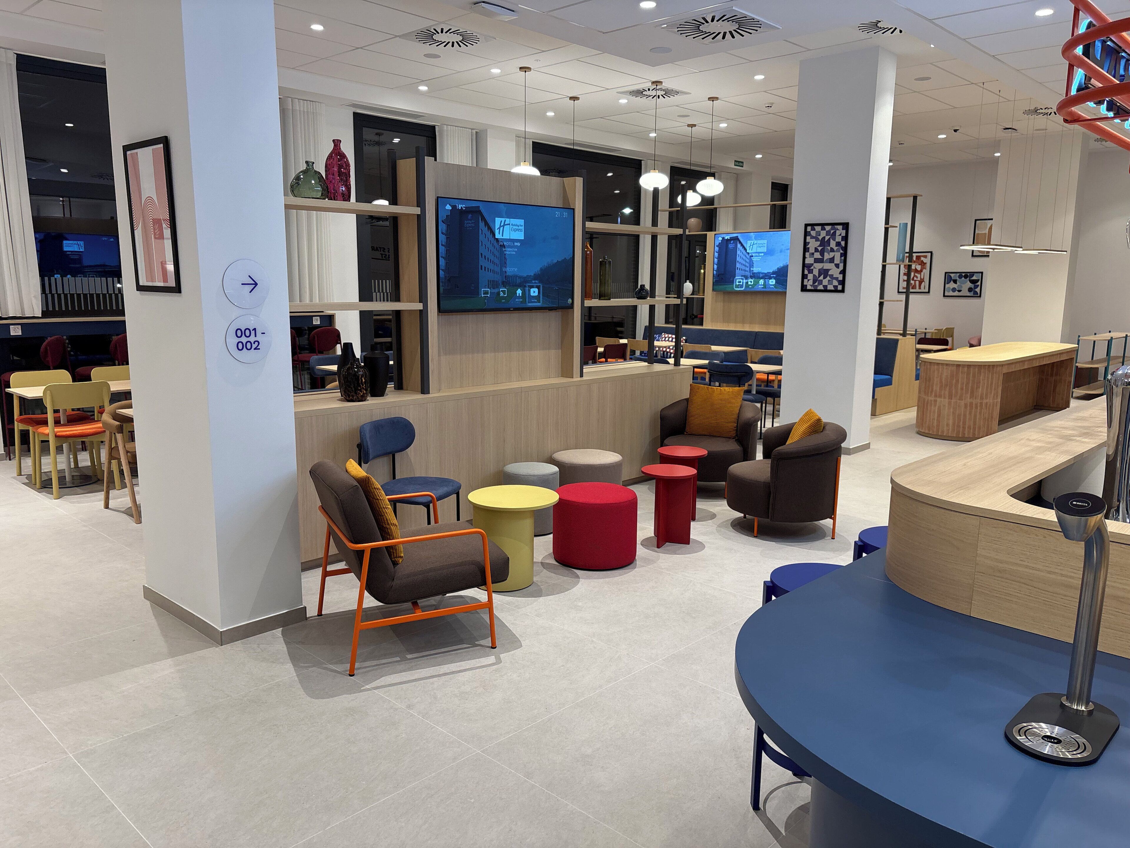 Un moderno vestíbulo de hotel con áreas de estar, un mostrador de recepción y pantallas digitales en las paredes.