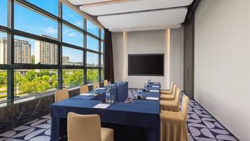 Ein Konferenzraum mit langem Tisch, Stühlen, einer Projektionsleinwand und Blick auf die Stadt durch große Fenster.