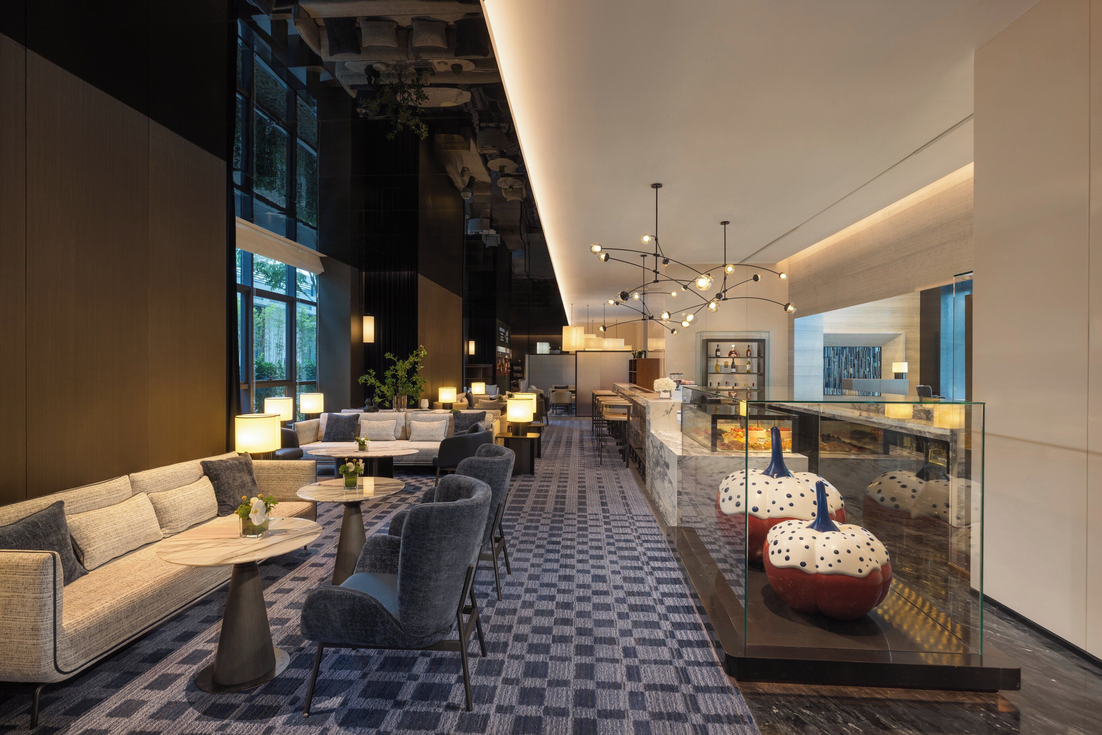 A modern hotel lobby with seating areas, a bar, and a glass display case with decorative items.