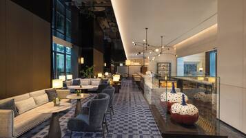 A modern hotel lobby with seating areas, a bar, and a glass display case with decorative items.