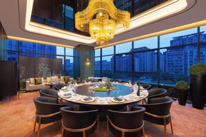 A modern dining room with a round table set for a meal, surrounded by chairs, and a large window offering a city view. - Crowne Plaza Suzhou Taihu Lake By Ihg (Suzhou)